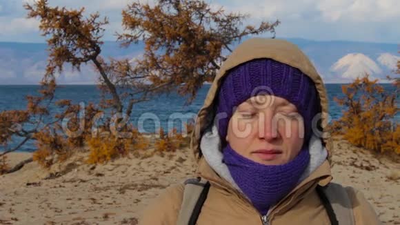 一个穿夹克衫带着兜帽在海边沉思的女孩的肖像视频的预览图