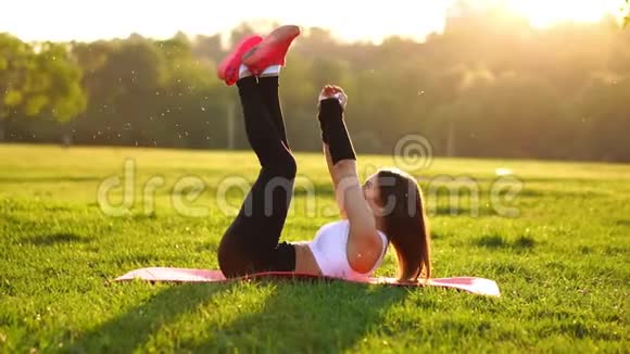 在夏季公园的健身垫上做腹部伸展运动的女人在日落时慢动作视频的预览图