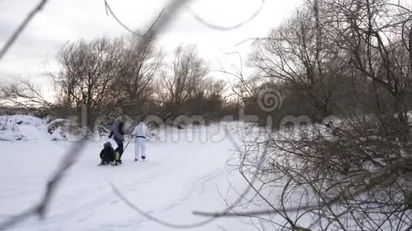 孩子们快乐的父母骑在雪橇上幸福的家庭在天然的溜冰场上休息阴沉的冬日慢动作视频的预览图