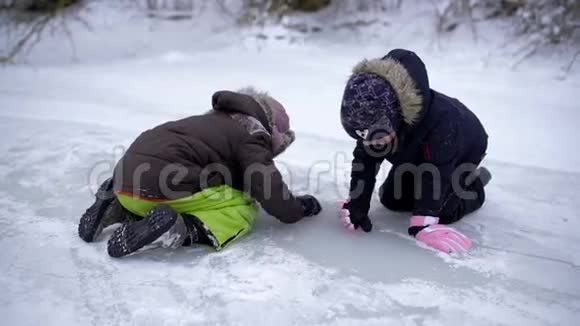 快乐有趣的孩子们坐在冰冻的湖面上擦冰两个人微笑着真的很开心阴郁的视频的预览图