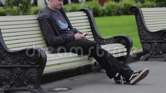 一个人坐在公园的长凳上疯狂地抬头看着电话视频的预览图