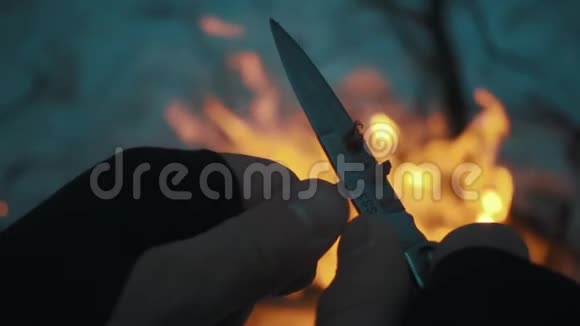 男人用刀把铅笔卷到篝火上视频的预览图