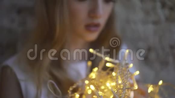 美丽少女靠墙少女手持花环圣诞灯视频的预览图