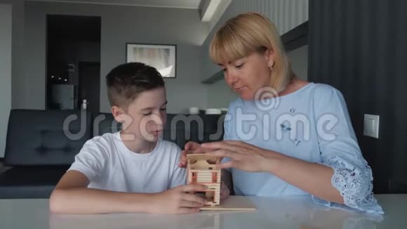 妈妈和儿子坐在一张桌子旁用木块收集一所房子梦想一个私人的家游戏和教学视频的预览图