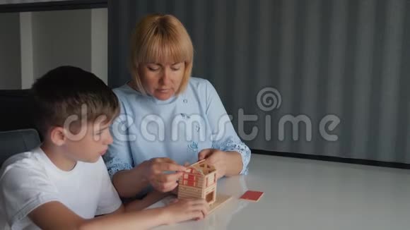 妈妈和儿子坐在一张桌子旁用木块收集一所房子梦想一个私人的家游戏和教学视频的预览图