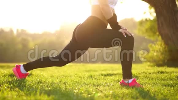 苗条的女运动员在公园里锻炼做膝盖弹跳或弓箭步穿着粉色运动鞋的日落脚视频的预览图