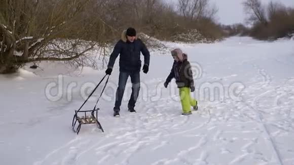 快乐的父亲和他的儿子雪橇玩他们一起在自然的溜冰场中快乐和快乐抓住雪橇的男孩慢慢视频的预览图