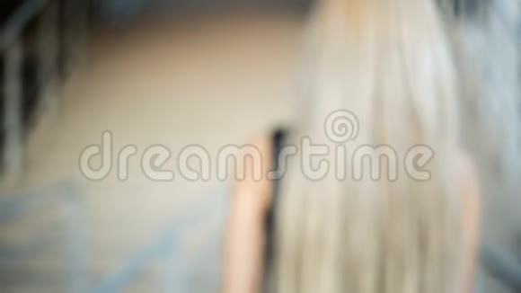 年轻的金发女人长着一头流动的长发爬上楼梯背面视频的预览图