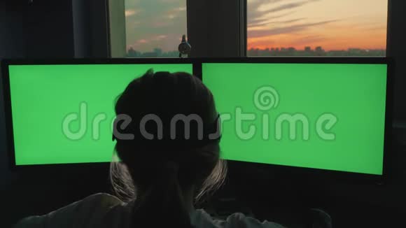 金发少女坐在粉红色日落背景下的绿色大屏幕显示器前的虚拟现实眼镜中视频的预览图