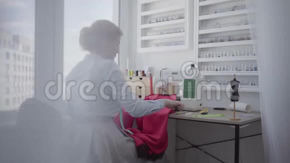 漂亮的红发女人坐在灯房靠窗的桌子边缝衣服女裁缝在家工作视频的预览图
