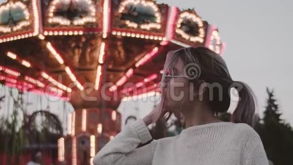 迷人的女孩戴着眼镜在游乐园的旋转木马附近摆姿势视频的预览图