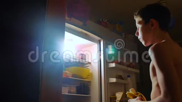 小男孩晚上从冰箱里吃饥饿和饕餮青少年男孩在生活方式之夜看冰箱视频的预览图