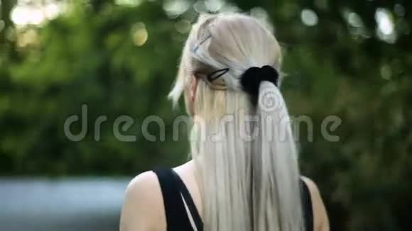 一位留着长发的年轻金发女子正在公园里散步视频的预览图