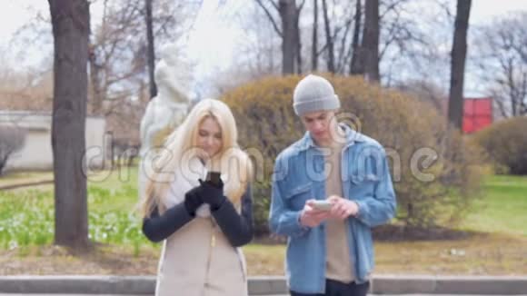 两个年轻人一个漂亮的金发女郎和她的朋友正在街上走着用着手机写消息视频的预览图