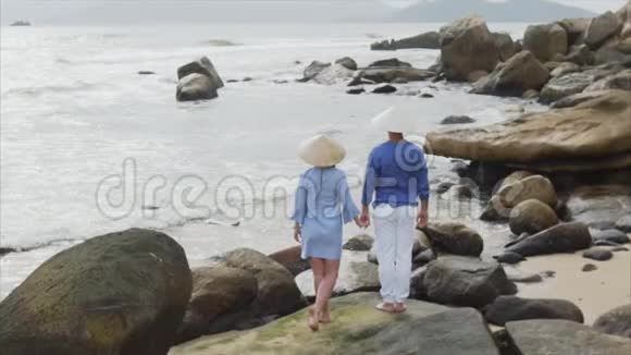 年轻漂亮的一对情侣戴着越南帽子穿着蓝色衣服手牵手在海边看着每一个人视频的预览图