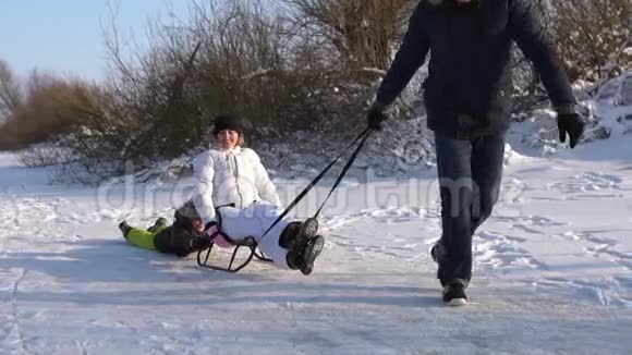 一个男人在雪橇上拉一个快乐的妻子和儿子男孩高兴地笑着走进镜头在大自然的命令下的晴天视频的预览图