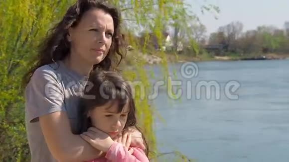 妈妈在河边拥抱她的女儿一个小女孩和她妈妈在水边家庭在露天视频的预览图