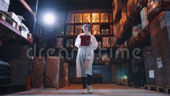漂亮的年轻女士走在巨大的储藏室的货架之间在工厂检查时做笔记视频的预览图