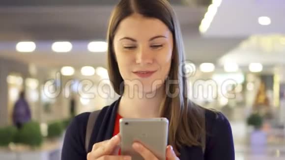 年轻漂亮的女人微笑着走在购物中心用她的智能手机和朋友聊天视频的预览图