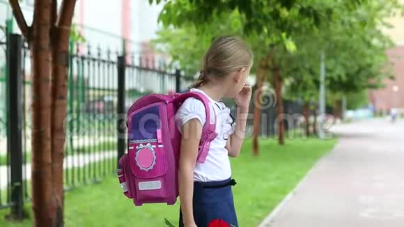 一个年轻漂亮的女孩背着书包站在学校附近带着鲜花阳光明媚回到学校女学生去学习视频的预览图