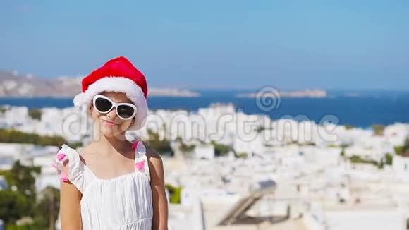 迷人的女孩穿着白色连衣裙和红色帽子户外背景的Mykonos典型的希腊传统街上的孩子视频的预览图
