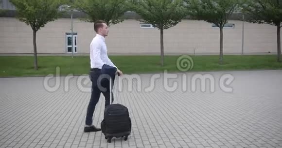 在工作的商人穿着白色衬衫的英俊青年提着手提箱从机场走出来视频的预览图