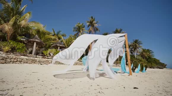 婚礼拱门在靠近海洋的海滩上装饰着鲜花她的白色和蓝色的画布在风中飘扬装饰视频的预览图