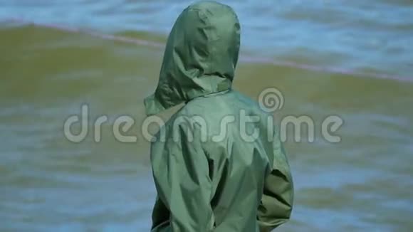 慢动作这个男孩是一个十几岁的孩子穿着一件灰绿色的夹克站在湖岸上享受着清新的微风他转身视频的预览图