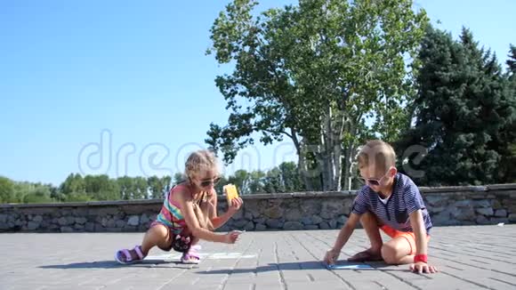 孩子们一个男孩和一个女孩戴着太阳镜用彩色蜡笔在沥青上画画街道瓷砖炎炎夏日视频的预览图