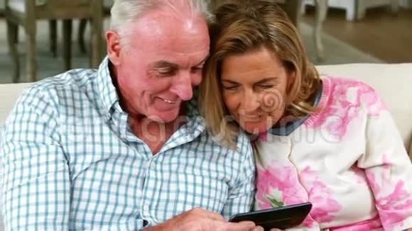 微笑的老夫妇在客厅里看着手机拍摄的照片视频的预览图