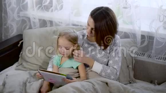 快乐的一家人在睡觉互相享受漂亮的年轻妈妈正在给她可爱的小女儿读一本书妇女视频的预览图