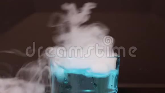 在一杯蓝色的水中干冰在黑色的背景上产生白色的烟雾视频的预览图