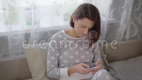 穿着灰色睡衣的短发迷人的黑发女人正坐在卧室的沙发上用她的发型视频的预览图