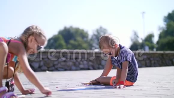 孩子们一个男孩和一个女孩戴着太阳镜用彩色蜡笔在沥青上画画街道瓷砖炎炎夏日视频的预览图