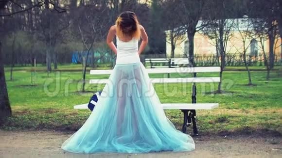 穿着白色和蓝色裙子的漂亮女孩站在公园路长凳旁用可见的内衣和谈话来调整衣服视频的预览图
