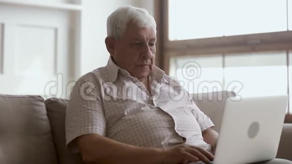 坐在家里的沙发上用笔记本电脑的老人视频的预览图