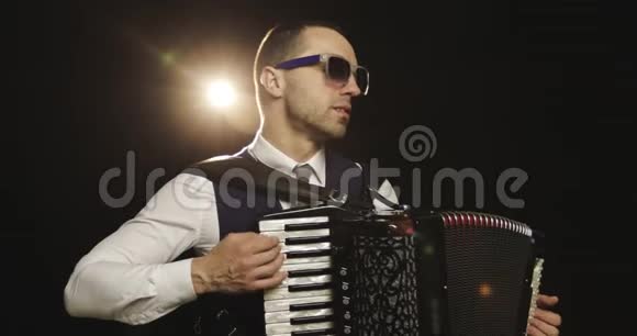一个穿着白色衬衫的时尚音乐家在工作室里用黑色背景演奏手风琴视频的预览图