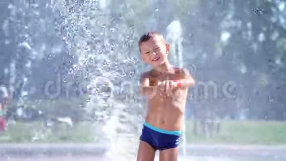 七岁的快乐男孩穿着泳衣在喷水池里嬉戏城市里阳光明媚的夏日视频的预览图