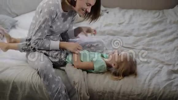 幸福的一家人在家里的床上玩耍和拥抱姐姐在开玩笑地摇着她的小妹妹他们俩视频的预览图