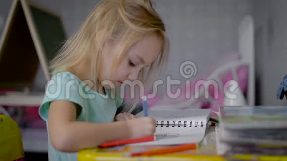 在托儿所的那个女孩在一张桌子上婴儿画一本素描本手里拿着一支彩色的毛毡尖笔在一个视频的预览图