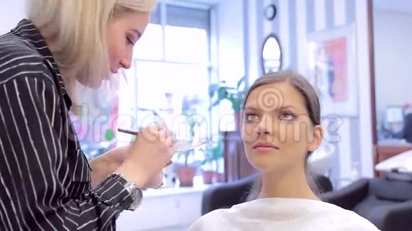 化妆师用刷子和海绵在年轻女子脸上涂抹粉底视频的预览图