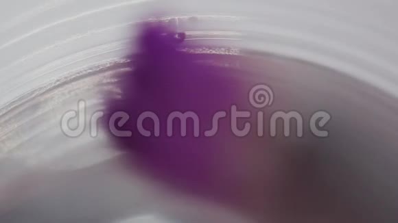 将带有紫色油漆的画笔浸入水杯中视频的预览图