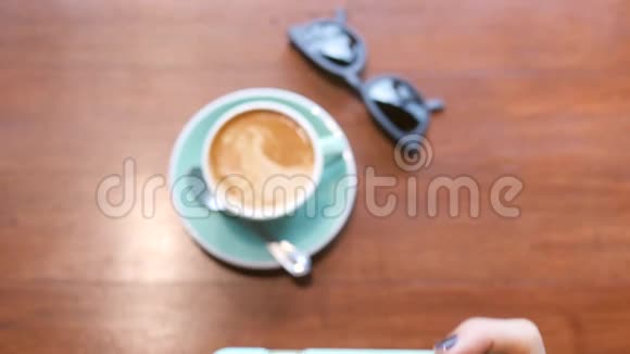 年轻的少女在杯中拍咖啡壶在木桌上拍太阳镜生活方式旅行视频的预览图
