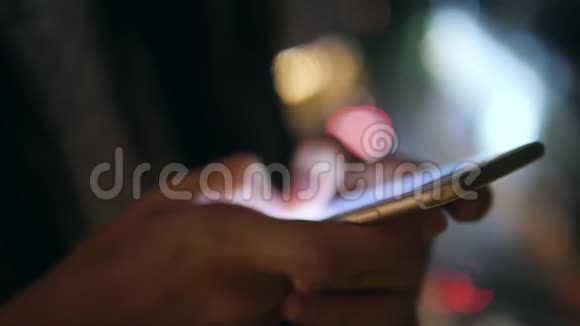 女性手使用智能手机与模糊的蓝色博克街城市夜路灯光背景4K泰国曼谷视频的预览图