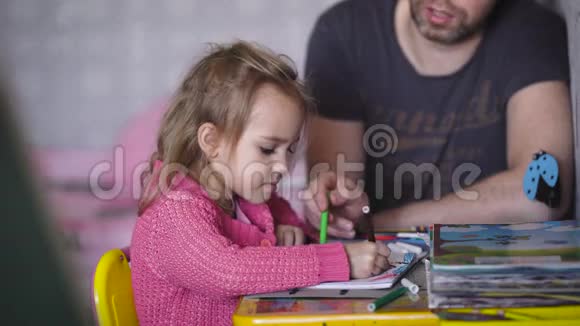 托儿所孩子和父亲在一张画桌旁那个和那个男人在一起的女孩画了一张绘画专辑在一张专辑里视频的预览图