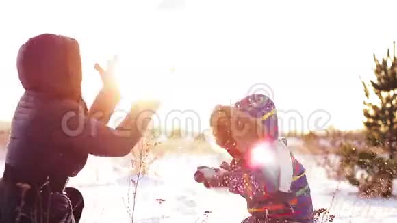 幸福的女人和孩子在冷杉附近日落时玩雪视频的预览图