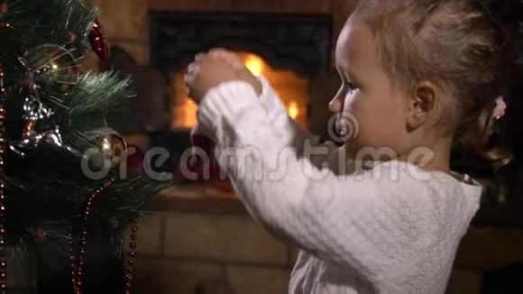 可爱的小女孩在黑暗的房间里用壁炉装饰圣诞树视频的预览图