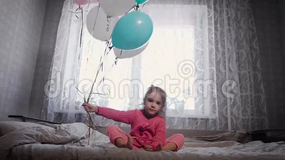 可爱的金发小女孩穿着粉红色的睡衣坐在父母的床上一边一边挥舞着视频的预览图