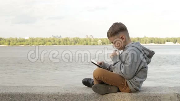 一个男孩正在海边的平板电脑上玩耍视频的预览图