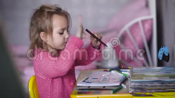 穿着粉红色开襟羊毛衫的漂亮小女孩正在幼儿园用彩色铅笔画插图小天才视频的预览图